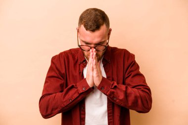 Beyaz tenli genç adam bej arka planda izole edilmiş dua ediyor, bağlılık gösteriyor, dindar biri ilahi ilham arıyor..