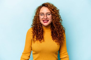 Mavi arka planda izole edilmiş genç beyaz kadın gülüyor ve gözlerini kapıyor, rahatlamış ve mutlu hissediyor..