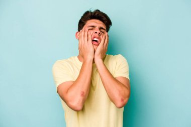 Kafkasyalı genç adam mavi arka planda izole edilmiş sızlanıyor ve ağlıyordu..