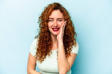 Mavi arka planda izole edilmiş genç beyaz kadın mutlu bir şekilde gülüyor ve ellerini karnının üstünde tutarak eğleniyor..