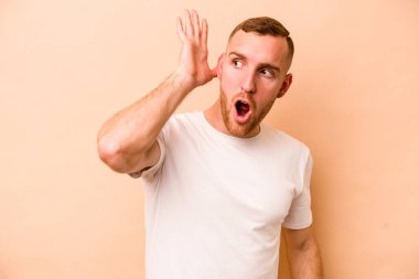 Beyazlı genç bir adam bej arka planda izole edilmiş bir şekilde bir dedikoduyu dinlemeye çalışıyor..