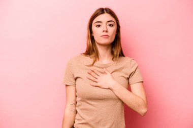 Pembe arka planda izole edilmiş genç beyaz kadın yemin ediyor, elini göğsüne koyuyor..