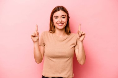 Pembe arka planda izole edilmiş genç beyaz kadın iki parmağı da boş bir alan gösteriyor..