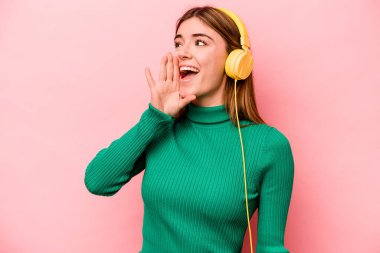 Pembe arka planda izole edilmiş müzik dinleyen beyaz bir kadın bağırıyor ve avuç içi kadar açık bir ağız tutuyor..