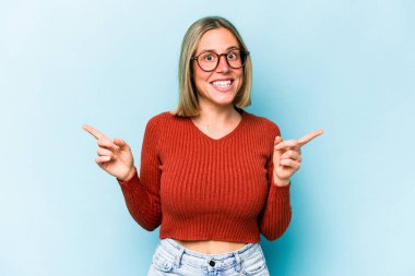Mavi arka planda izole edilmiş genç beyaz kadın farklı kopya alanlarını gösteriyor, birini seçiyor, parmaklarıyla gösteriyor..