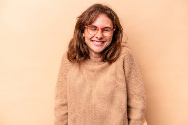 Beyaz tenli genç bir kadın bej arka planda izole edilmiş. Kahkahalar atıyor, gözlerini kapatıyor, rahatlıyor ve mutlu oluyor..