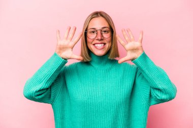 Pembe arka planda izole edilmiş genç beyaz kadın on numarayı elleriyle gösteriyor..