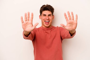 Beyaz arka planda izole edilmiş beyaz tenli genç adam on numarayı elleriyle gösteriyor..