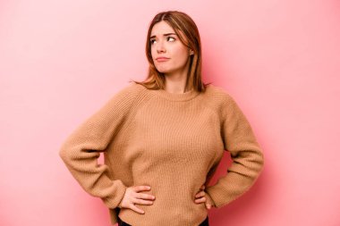 Pembe arka planda izole edilmiş genç beyaz kadın kafası karışmış, kuşkulu ve güvensiz hissediyor..