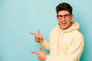 Kafkasyalı genç adam mavi arka planda izole edilmiş. İşaret parmağıyla işaret ettiği için heyecanlı..