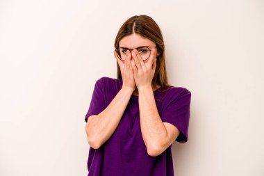 Beyaz arka planda izole edilmiş genç beyaz kadın kameraya parmaklarıyla göz kırpıyor, yüzünü kapatmaktan utanıyor..