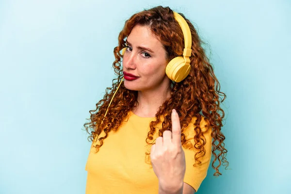 Νεαρή Κοκκινομάλλα Γυναίκα Ακούγοντας Μουσική Απομονωμένη Μπλε Φόντο Δείχνοντας Δάχτυλο — Φωτογραφία Αρχείου