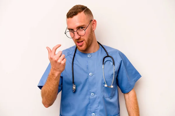 Young caucasian nurse man isolated on white background pointing with finger at you as if inviting come closer.