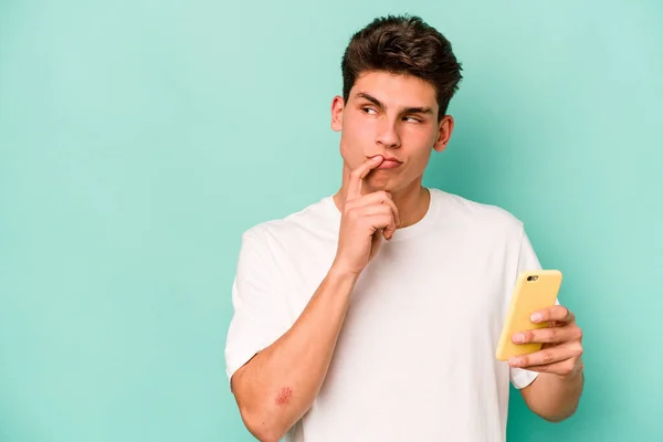 Młody Biały Mężczyzna Trzymając Telefon Komórkowy Odizolowany Niebieskim Tle Zrelaksowany — Zdjęcie stockowe