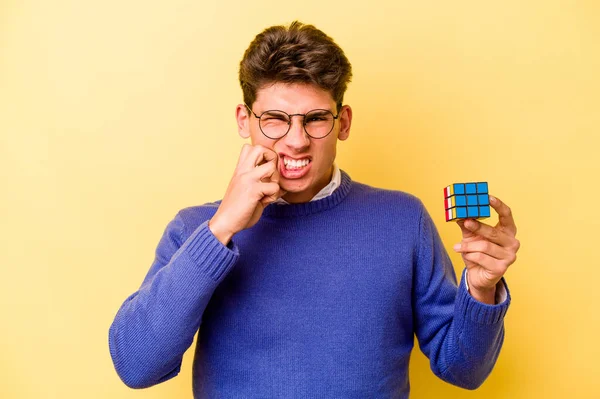 Mladý Běloch Drží Kostku Rubiks Izolovanou Žlutém Pozadí Kousání Nehty — Stock fotografie