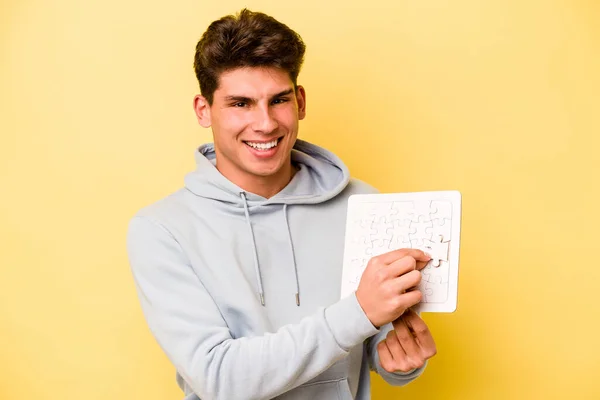黄色の背景に隔離されたパズルを持っている若い白人男性 — ストック写真