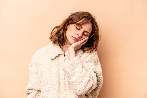 Молодая кавказская женщина изолирована на бежевом фоне, которой скучно, она устала и нуждается в отдыхе.