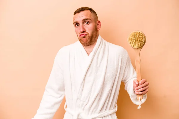 Young Caucasian Man Holding Back Scratcher Isolated Beige Background Shrugs — Stock Photo, Image