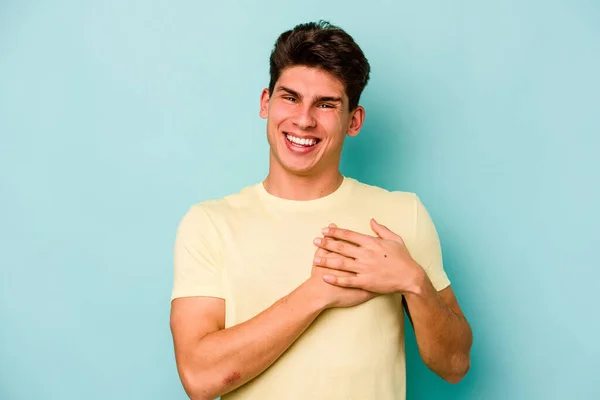 青い背景に孤立した若い白人男性が手を心に留めて笑い 幸福の概念 — ストック写真