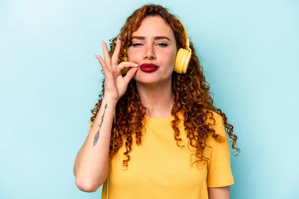 Young Ginger Woman Listening Music Isolated Blue Background Fingers Lips — Stock Photo, Image