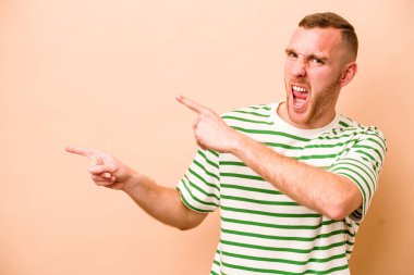 Beyaz tenli genç adam bej arka planda izole edilmiş ve işaret parmağıyla fotokopi alanını işaret ederek heyecan ve arzusunu ifade ediyor..