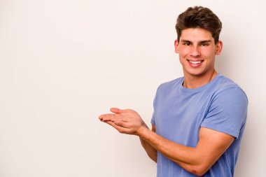 Beyaz arka planda izole edilmiş beyaz tenli genç bir adam palmiyesinde bir kopya alanı tutuyor..