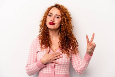 Beyaz arka planda izole edilmiş genç beyaz kadın yemin ediyor, elini göğsüne koyuyor..