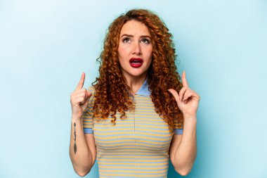 Genç, beyaz, mavi arka planda izole edilmiş bir kadın ağzı açık, üst tarafı işaret ediyor..