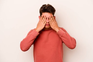 Beyaz arka planda izole edilmiş genç beyaz bir adam elleriyle gözlerini kapatmaktan korkuyor..