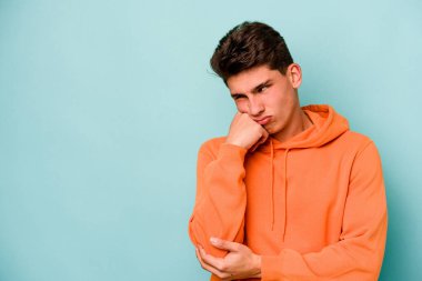 Mavi arka planda izole edilmiş, üzgün ve dalgın hisseden, kopyalama alanına bakan genç beyaz bir adam..