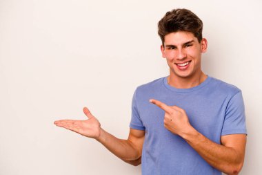 Beyaz arka planda izole edilmiş genç beyaz bir adam, palmiye üzerinde bir fotokopi alanı tutarken heyecanlı..