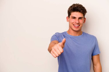 Beyaz arka planda izole edilmiş genç beyaz adam gülümsüyor ve başparmağını kaldırıyor.