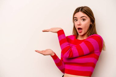 Beyaz arka planda izole genç beyaz kadın şok ve hayret içinde elleri arasında bir kopya alanı tutuyor.