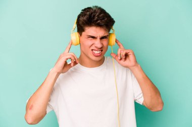 Müzik dinleyen beyaz bir adam mavi arka planda izole edilmiş kulakları elleriyle kapatıyor..