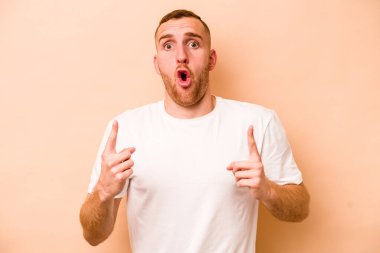 Beyazlı genç bir adam bej arka planda izole edilmiş. Ağzı açık, üst tarafı işaret ediyor..