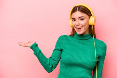 Pembe arka planda müzik dinleyen beyaz bir kadın bir avuç içinin fotokopi çektiğini ve başka bir elini belinde tuttuğunu gösteriyor..