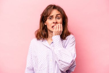 Pembe arka planda izole edilmiş, tırnak yiyen, gergin ve endişeli bir beyaz kadın..