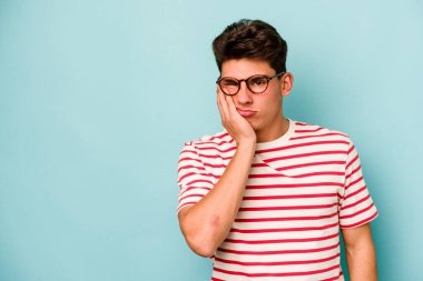 Mavi arka planda izole edilmiş, üzgün ve dalgın hisseden, kopyalama alanına bakan genç beyaz bir adam..