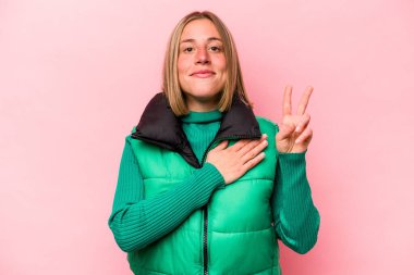 Pembe arka planda izole edilmiş genç beyaz kadın yemin ediyor, elini göğsüne koyuyor..