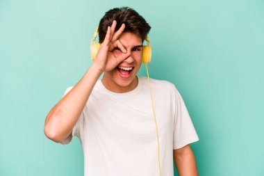 Mavi arka planda izole edilmiş müzik dinleyen beyaz bir adam heyecanlı..