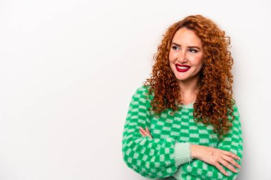 Beyaz arka planda soyutlanmış beyaz tenli genç bir kadın kollarını kavuşturarak gülümsüyor..