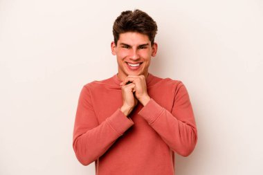 Beyaz arka planda izole genç beyaz adam ellerini çenesinin altında tutuyor, mutlu bir şekilde yana bakıyor..