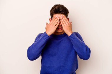 Beyaz arka planda izole edilmiş genç beyaz bir adam elleriyle gözlerini kapatmaktan korkuyor..