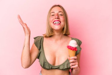 Genç beyaz kadın bikini giyiyor ve pembe arka planda izole edilmiş dondurma tutuyor. Hoş bir sürpriz, heyecanlı ve el kaldırıyor..