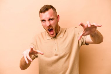 Beyazlı genç bir adam bej arka planda izole edilmiş pençelerini kedi taklidi yaparken gösteriyor, agresif bir hareket..