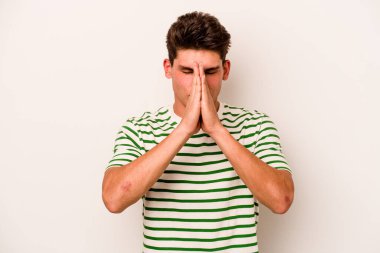 Beyaz arka planda izole edilmiş genç beyaz bir adam el ele tutuşup, ağız kenarında dua ediyor, kendinden emin..