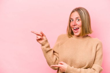 Pembe arka planda izole edilmiş genç beyaz kadın işaret parmaklarıyla fotokopi alanını işaret ederek heyecan ve arzusunu ifade ediyor..