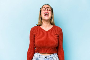 Genç beyaz kadın mavi arka planda izole edilmiş rahat ve mutlu bir şekilde gülüyor, boynunda dişlerini gösteriyor..