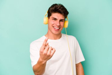 Kafkasyalı genç adam, mavi arka planda izole edilmiş müzik dinliyor. Sanki seni davet ediyormuş gibi parmakla işaret ediyor..
