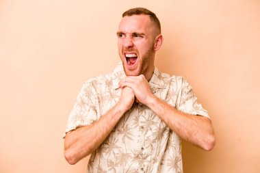 Beyaz tenli genç adam bej arka planda izole edilmiş ellerini çenesinin altında tutuyor, mutlu bir şekilde yana bakıyor..